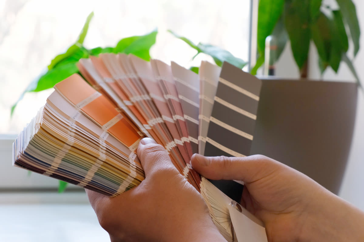 A fan of paint colour swatches held open against a wall