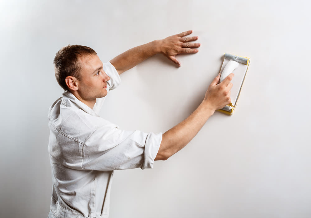 A painter sanding a filled wall flat by hand